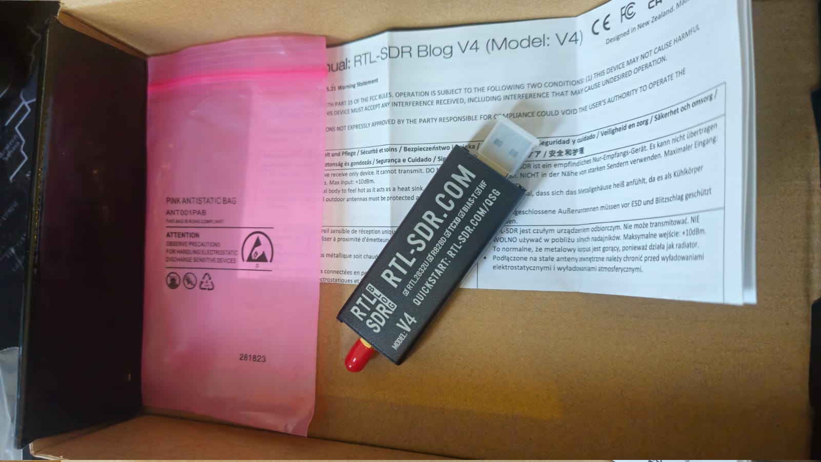 Dongle RTL-SDR Blog V4 sobre o manual, com RTL2832U, R828D, TCXO, bias-T e HF marcados na serigrafia da caixa de alumínio